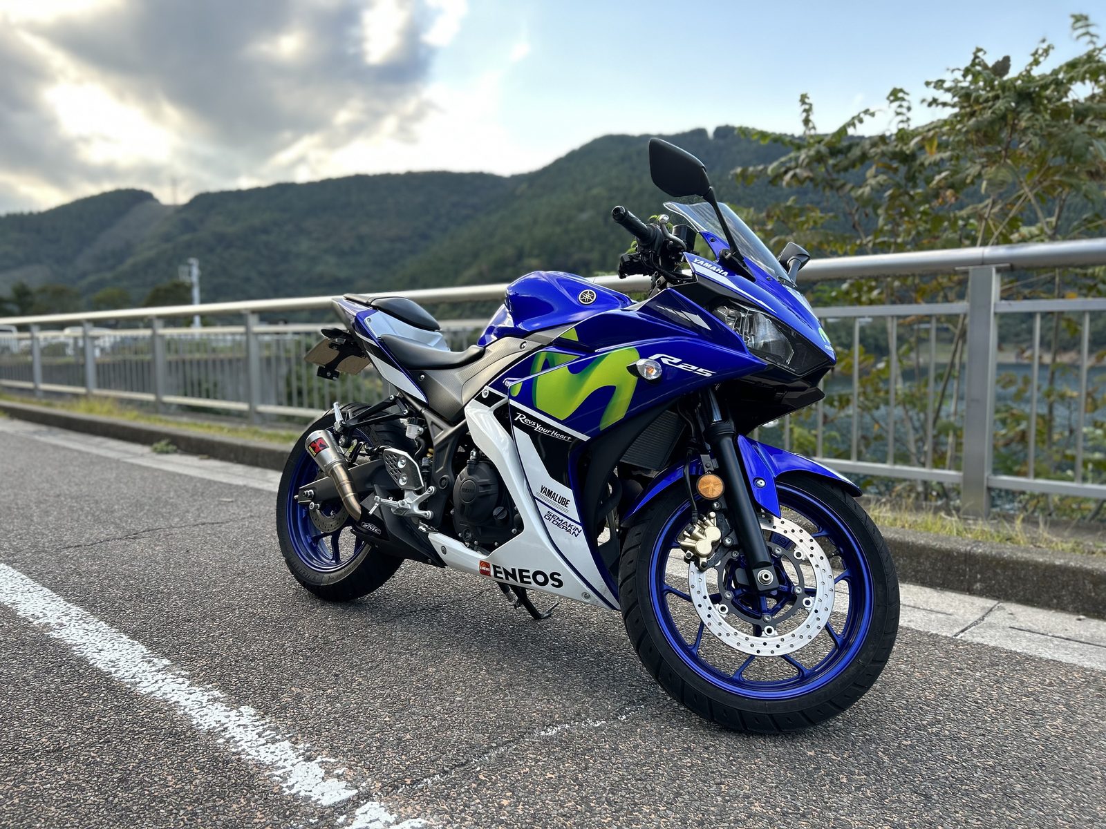 宮ヶ瀬湖畔の道路脇に停めた愛車。ガードレールの向こうに宮ヶ瀬湖と山並みが広がる。15時36分、薄雲の合間から日が差していた