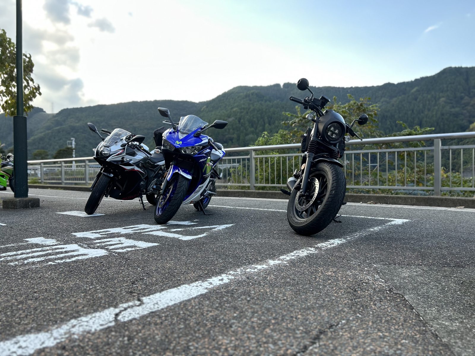 低い位置から3台を見上げるように撮った1枚。左から白黒のスズキ、青いR25、黒いネイキッド。奥に山並みが広がる